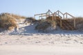 Wooden stairway on white sand beach with grass. Ocean coast landscape. Footpath on white sand and wooden outdoor stairs. Royalty Free Stock Photo