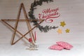 Wooden star with garland lights and Merry Christmas inscription on white wooden wall background. Golden stars, red pillows Royalty Free Stock Photo