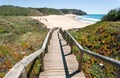 Wooden steps to the sunny beach in Portugal town. Ocean waters and green hills over peaceful seaside at sunny day Royalty Free Stock Photo