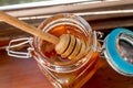 Wooden stick for honey lies in a jar of golden sunny sweet honey. Glass jar stands on the table