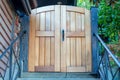 Wooden sturdy gate on front door entrace to house or home with stoop or stairs and black metal hand rails