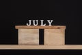 Wooden summer calendar months - July. Wooden letters on stand on black background