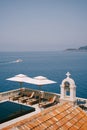 Budva, Montenegro - 01 august 2020: Wooden sun loungers under white beach umbrellas, near the pool and church Royalty Free Stock Photo