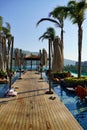 Wooden sunbeds and parasols on wooden deck nearby swimming pool in the evening. The outdoor recreation in luxury hotel. Royalty Free Stock Photo