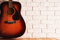 Wooden table with an acoustic guitar and white bricks background Royalty Free Stock Photo