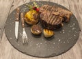 On wooden table background juicy beef steak medium rare on a stone baked potatoes and barbecue sauce and large sea salt with fork Royalty Free Stock Photo