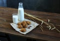 On a wooden table is a bottle and a glass of milk, cookies with chocolate on a plate, spikelets of wheat