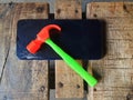 on the wooden table a broken cell phone and an orange toy hammer with a green handle Royalty Free Stock Photo