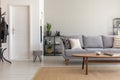 Wooden table on carpet in front of grey sofa in minimal living room interior with door