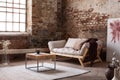 Wooden table on carpet next to grey settee in wabi sabi living room interior with poster and window