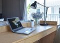 Wooden table with computer notebook,pencil,lamp and artificial flowers in modern working area at home