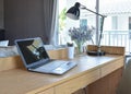 Wooden table with computer notebook,pencil,lamp and artificial flowers in modern working area at home