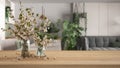 Wooden table, desk or shelf close up with branches of cherry blossoms in glass vase over blurred view of modern kitchen and living