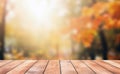 Wooden table in front of blurred autumn forest background with bokeh sunlight.