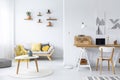 Wooden table in front of sofa in white apartment interior with posters and chair at desk. Real photo