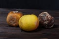 on a wooden table are fruits. in the foreground is a ripe green apple, behind it are black and brown rotten apples