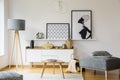 Wooden table and grey pouf in bright flat interior with posters