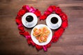 On the wooden table, inside the heart of the rose petals are two cups of coffee and a plate with cookies in the form of hearts. Royalty Free Stock Photo