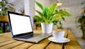 Wooden table with laptop with blank white screen mockup, cup of coffee and potted plant. Cozy workspace in a cafe or office. Royalty Free Stock Photo