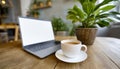 Wooden table with laptop with blank white screen mockup, cup of coffee and potted plant. Cozy workspace in a cafe or office. Royalty Free Stock Photo