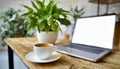 Wooden table with laptop with blank white screen mockup, cup of coffee and potted plant. Cozy workspace in a cafe or office. Royalty Free Stock Photo