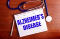 On a wooden table lie a stethoscope and a notebook with the words ALZHEIMERS DISEASE. Medical concept Royalty Free Stock Photo
