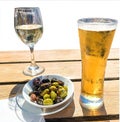 Wooden table with light beer in the mug , white wine in the glass and olives in white plate