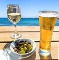 Wooden table with light beer in the mug , white wine in the glass and olives in white plate