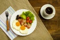 On a wooden table on a linen napkin, a plate with fried eggs with bacon and a cup of coffee. Royalty Free Stock Photo