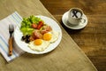 On a wooden table on a linen napkin, a plate with fried eggs with bacon and a cup of coffee. Royalty Free Stock Photo