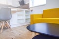 Wooden table in living room. Yellow sofa, wooden chair and white table in background. Background is blur