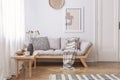 Wooden table next to beige settee with blanket in bright living room interior with poster. Real photo Royalty Free Stock Photo