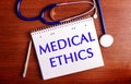 On a wooden table are a pen, a stethoscope, and a notebook labeled MEDICAL ETHICS. Medical concept Royalty Free Stock Photo