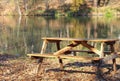 Wooden table with picnic benches in the open air on the background of fallen oak leaves near a forest lake Royalty Free Stock Photo