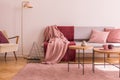 Wooden table on pink carpet in front of grey settee in living room interior with lamp. Real photo Royalty Free Stock Photo