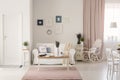 Wooden table on pink rug in white living room interior with rocking chair next to couch. Real photo Royalty Free Stock Photo