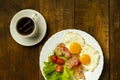 On a wooden table is a plate with fried eggs and a cup of coffee. Royalty Free Stock Photo