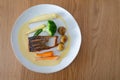 On a wooden table, a plate of pan-fried salmon with new potatoes, carrots, broccoli, baby sweetcorn, and white wine sauce