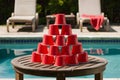 Wooden table with red cup pyramid by pool, lounge chairs with red towel Royalty Free Stock Photo