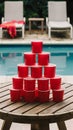 Wooden table with red cup pyramid by pool, lounge chairs with red towel Royalty Free Stock Photo