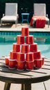 Wooden table with red cup pyramid by pool, lounge chairs with red towel Royalty Free Stock Photo