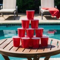 Wooden table with red cup pyramid by pool, lounge chairs with red towel Royalty Free Stock Photo