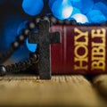 On a wooden table are a rosary with the crucifixion of Jesus Christ, a red book - the Holy Bible. Dark blue background with Royalty Free Stock Photo