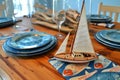 wooden table with a sailboat model, blue plates, and fishpatterned napkins