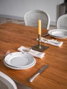 Wooden table setting for two persons, with plates, cutlery and old candlestick with candle. Interior of living room