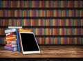 Wooden table with a stack of colored books and tablet. Blurred background with bookshelves. Table top with books in the library Royalty Free Stock Photo