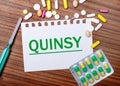 On a wooden table, a syringe, pills and a sheet of paper with the inscription QUINSY. Medical concept