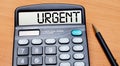 On a wooden table there is a black pen and a calculator with the text URGENT. Business concept Royalty Free Stock Photo