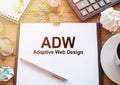 On a wooden table there is an office sheet of paper with the text ADW - Adaptive Web Design. Business workspace with calculator,