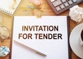 On a wooden table there is an office sheet of paper with the text INVITATION FOR TENDER. Business workspace with calculator,